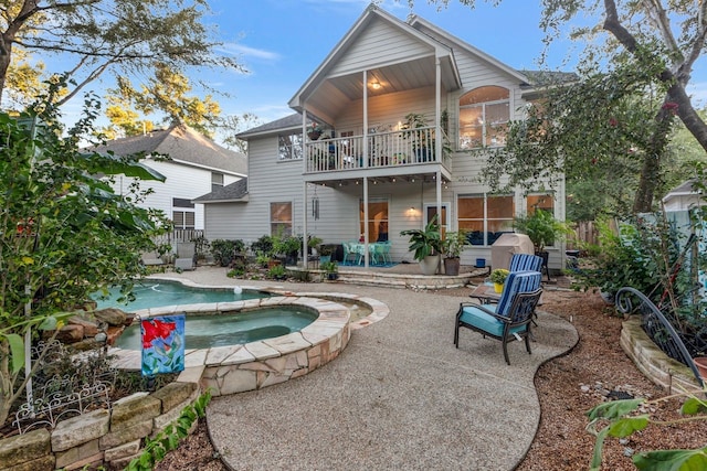 back of property featuring an in ground hot tub, a balcony, and a patio area