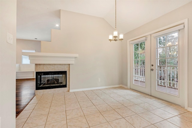 unfurnished living room with french doors, a notable chandelier, vaulted ceiling, a fireplace, and light tile patterned floors