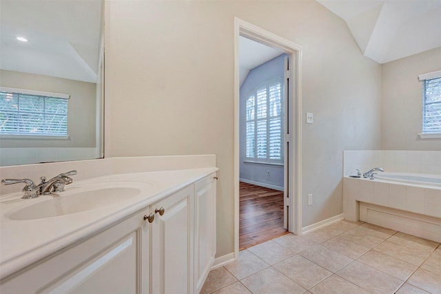 bathroom featuring tiled bath, tile patterned flooring, vanity, and lofted ceiling