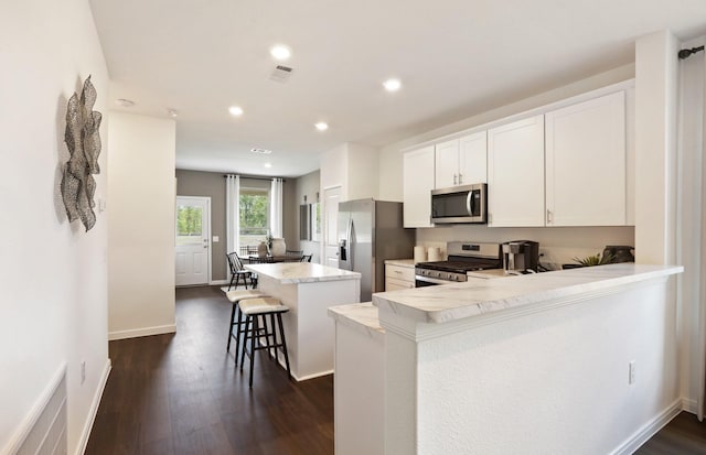 kitchen with a breakfast bar, a center island, kitchen peninsula, white cabinetry, and stainless steel appliances