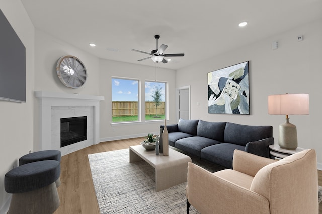 living room featuring a tile fireplace, light hardwood / wood-style floors, and ceiling fan