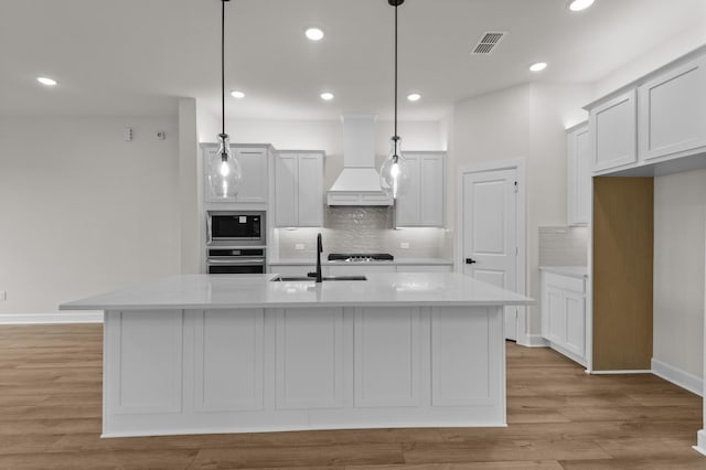 kitchen featuring appliances with stainless steel finishes, custom exhaust hood, sink, hanging light fixtures, and an island with sink