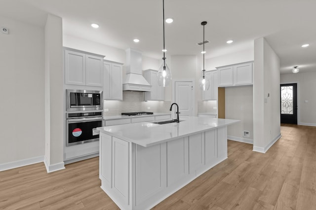 kitchen with a center island with sink, custom exhaust hood, sink, and appliances with stainless steel finishes