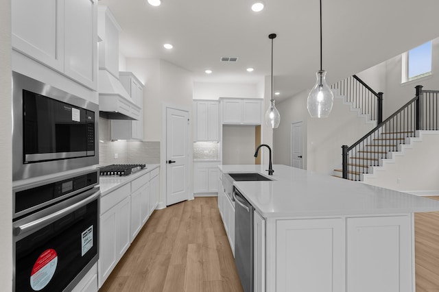 kitchen featuring decorative backsplash, sink, decorative light fixtures, white cabinetry, and an island with sink