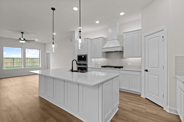 kitchen featuring custom exhaust hood, backsplash, a center island with sink, black gas stovetop, and decorative light fixtures