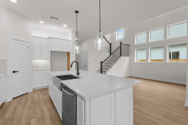 kitchen featuring white cabinets, stainless steel dishwasher, a kitchen island with sink, and sink