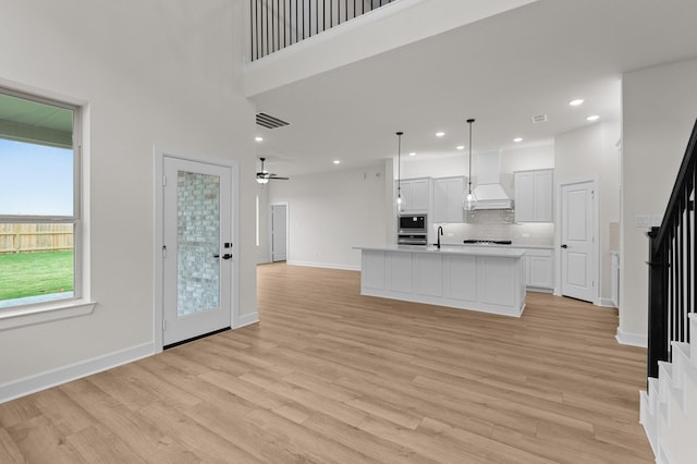 kitchen featuring pendant lighting, premium range hood, light hardwood / wood-style flooring, an island with sink, and white cabinetry