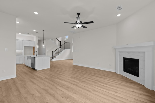 unfurnished living room featuring a premium fireplace, ceiling fan, sink, and light hardwood / wood-style floors