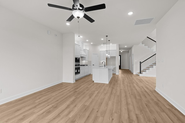 unfurnished living room featuring ceiling fan with notable chandelier, light hardwood / wood-style floors, and sink