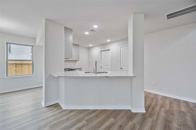 kitchen featuring kitchen peninsula, light stone countertops, light wood-type flooring, tasteful backsplash, and sink