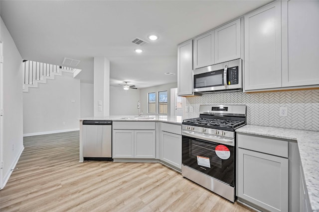 kitchen with light stone countertops, appliances with stainless steel finishes, backsplash, ceiling fan, and sink