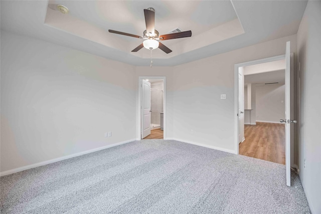 unfurnished bedroom featuring a tray ceiling, ceiling fan, and light colored carpet