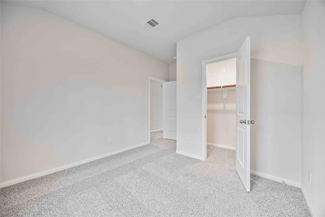 unfurnished bedroom featuring a walk in closet, light carpet, a closet, and vaulted ceiling