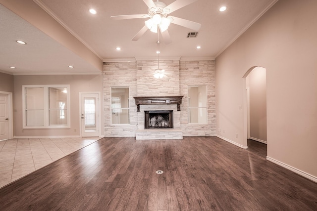 unfurnished living room with a stone fireplace, ceiling fan, crown molding, and wood-type flooring