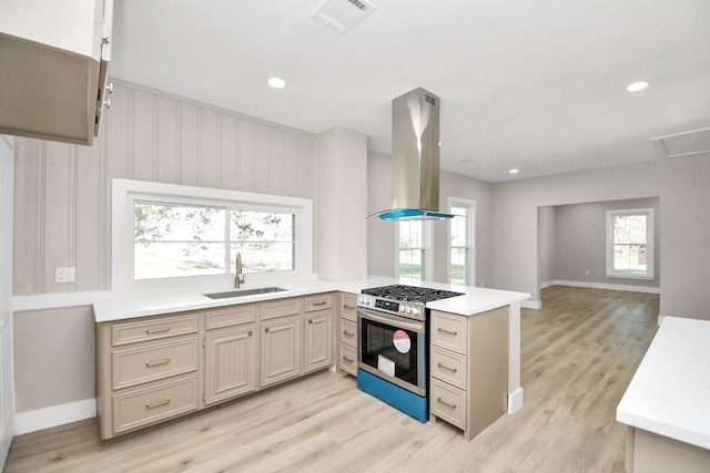 kitchen with kitchen peninsula, stainless steel gas range oven, island range hood, sink, and light hardwood / wood-style floors