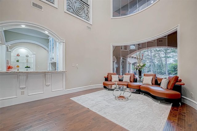 living room featuring visible vents, a towering ceiling, baseboards, and wood finished floors