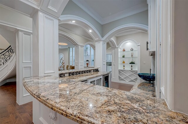 bar with light stone counters, ornate columns, beverage cooler, crown molding, and white cabinets