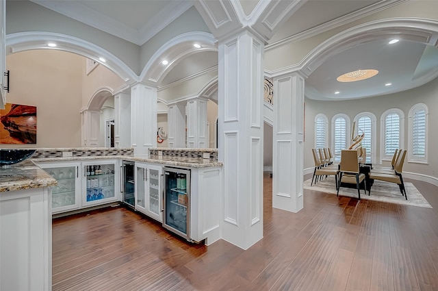 bar with tasteful backsplash, decorative columns, wine cooler, crown molding, and white cabinets