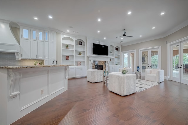 living area with ornamental molding, a glass covered fireplace, dark wood-style floors, french doors, and ceiling fan