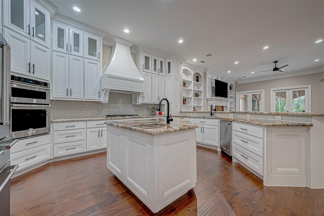 kitchen with white cabinets, custom exhaust hood, an island with sink, and light stone countertops