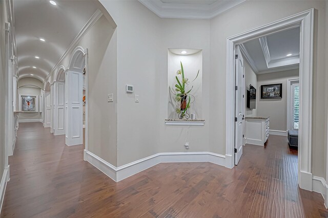 hallway featuring dark wood-style floors, baseboards, ornate columns, arched walkways, and crown molding