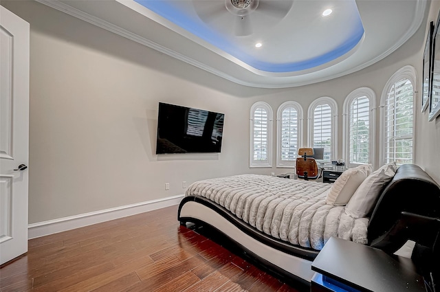 bedroom with a raised ceiling, wood finished floors, crown molding, baseboards, and ceiling fan