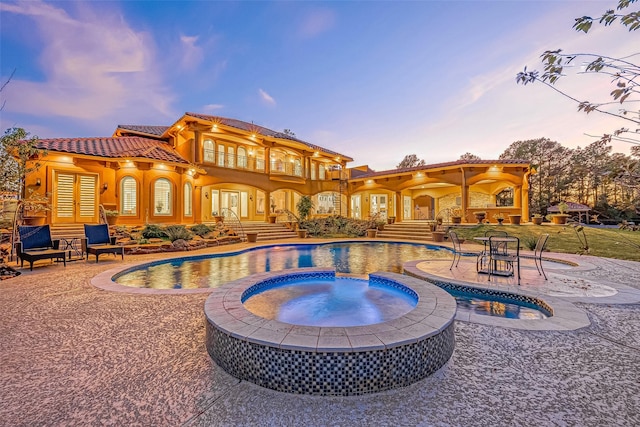 pool at dusk featuring an outdoor pool, a patio, and an in ground hot tub