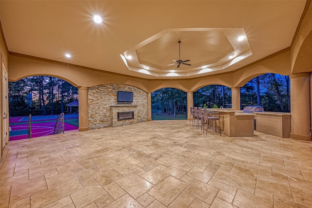 view of patio featuring outdoor dry bar, a ceiling fan, grilling area, an outdoor stone fireplace, and an outdoor kitchen