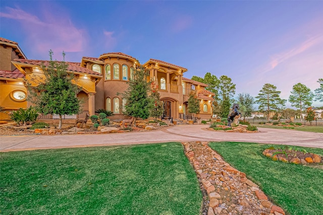 mediterranean / spanish-style house featuring stucco siding, a lawn, a tile roof, and curved driveway