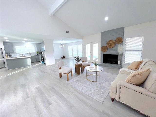 living room featuring a large fireplace, an inviting chandelier, light hardwood / wood-style flooring, beamed ceiling, and high vaulted ceiling