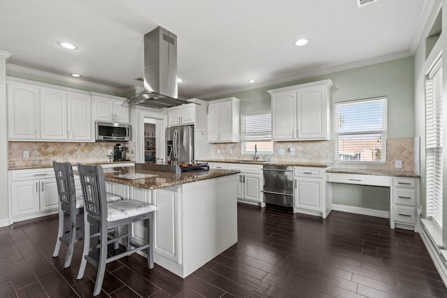 kitchen featuring stainless steel appliances, island range hood, white cabinetry, dark stone countertops, and a kitchen island