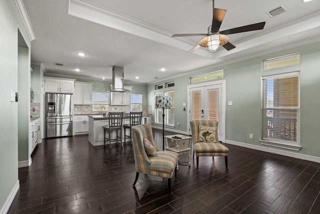 living room with french doors, ornamental molding, a textured ceiling, a raised ceiling, and ceiling fan