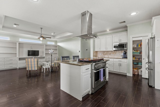 kitchen with appliances with stainless steel finishes, dark stone counters, island range hood, ceiling fan, and white cabinets