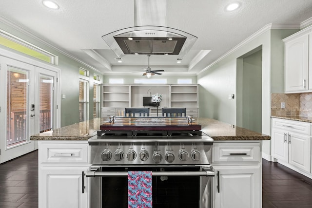 kitchen with white cabinetry, a raised ceiling, island exhaust hood, dark stone counters, and range with two ovens