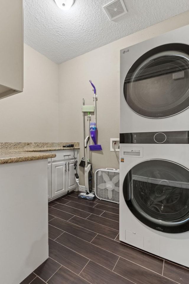 clothes washing area with cabinets, stacked washing maching and dryer, and a textured ceiling