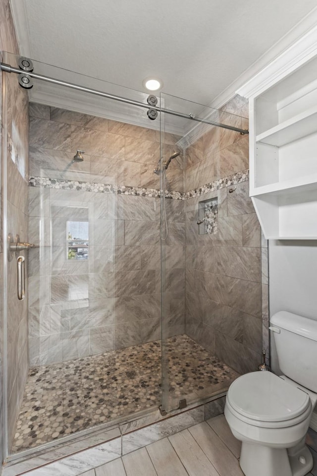 bathroom featuring toilet, a shower with shower door, and ornamental molding