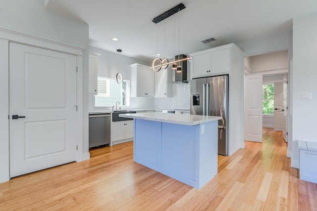 kitchen featuring a center island, hanging light fixtures, light wood-type flooring, appliances with stainless steel finishes, and white cabinetry