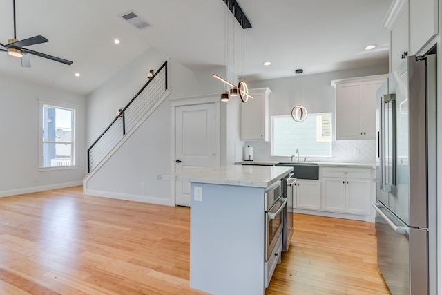 kitchen with high end refrigerator, white cabinetry, a center island, and hanging light fixtures