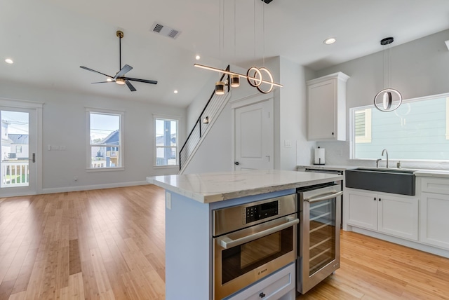 kitchen featuring white cabinets, sink, wine cooler, decorative light fixtures, and a kitchen island