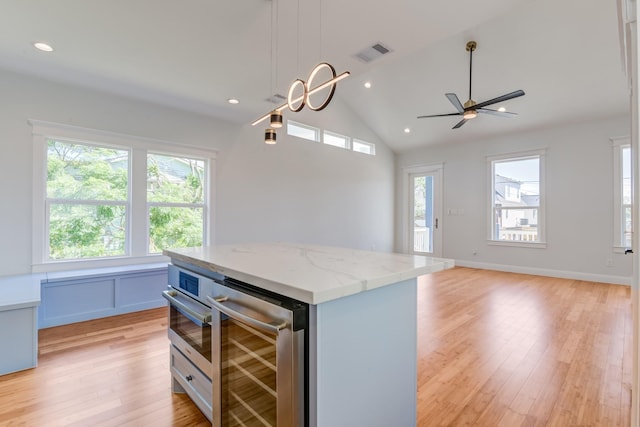 kitchen with wine cooler, light stone countertops, decorative light fixtures, a kitchen island, and white cabinetry