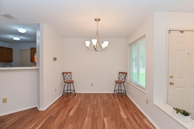 unfurnished dining area with hardwood / wood-style floors, a textured ceiling, and an inviting chandelier