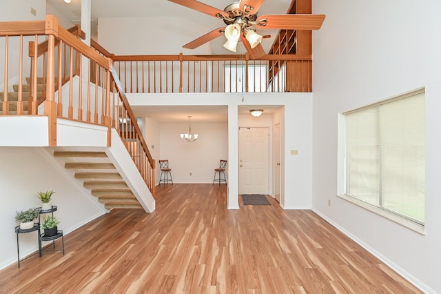 entrance foyer with hardwood / wood-style floors, ceiling fan with notable chandelier, and a towering ceiling