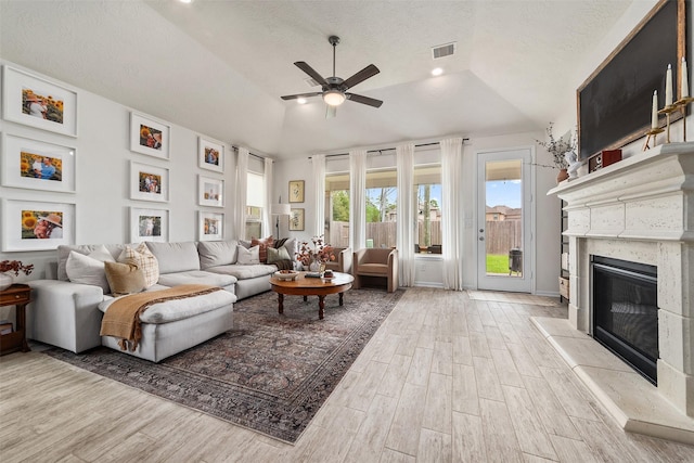 living room with a high end fireplace, a raised ceiling, vaulted ceiling, ceiling fan, and a textured ceiling