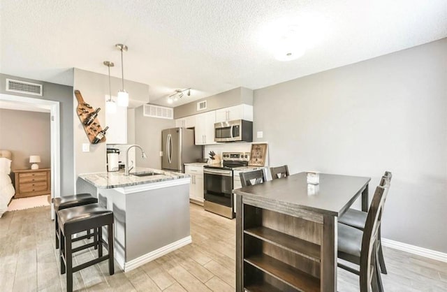 kitchen featuring sink, kitchen peninsula, decorative light fixtures, white cabinetry, and stainless steel appliances