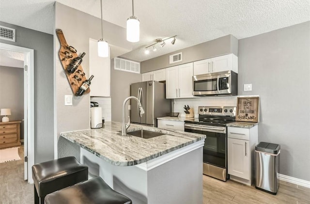 kitchen featuring hanging light fixtures, stainless steel appliances, light hardwood / wood-style flooring, kitchen peninsula, and white cabinets