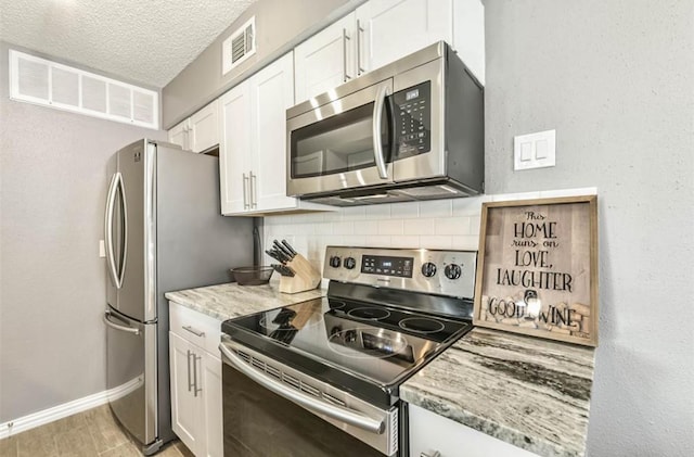 kitchen featuring appliances with stainless steel finishes, a textured ceiling, white cabinetry, and backsplash