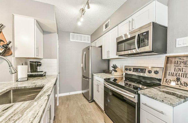 kitchen featuring light stone counters, a textured ceiling, stainless steel appliances, sink, and white cabinetry