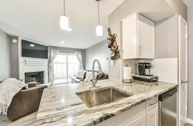 kitchen with sink, white cabinets, stainless steel dishwasher, and a brick fireplace