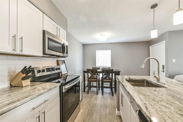 kitchen with pendant lighting, sink, tasteful backsplash, white cabinetry, and stainless steel appliances