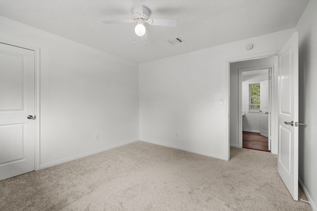 unfurnished bedroom with ceiling fan, light colored carpet, and a textured ceiling